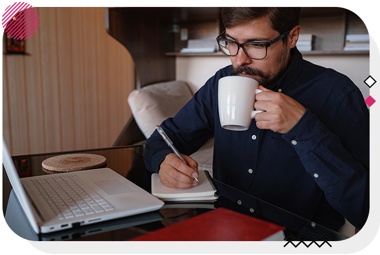 Man sipping from a mug and writing notes in a notebook